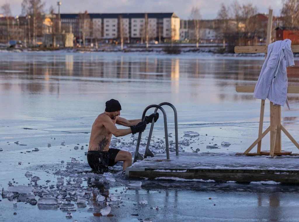 Чоловік занурюється у воду взимку.