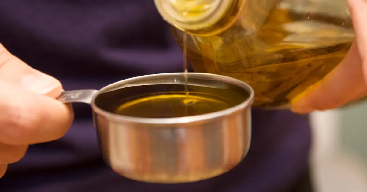 людина наливає олію з пляшки в посуд
